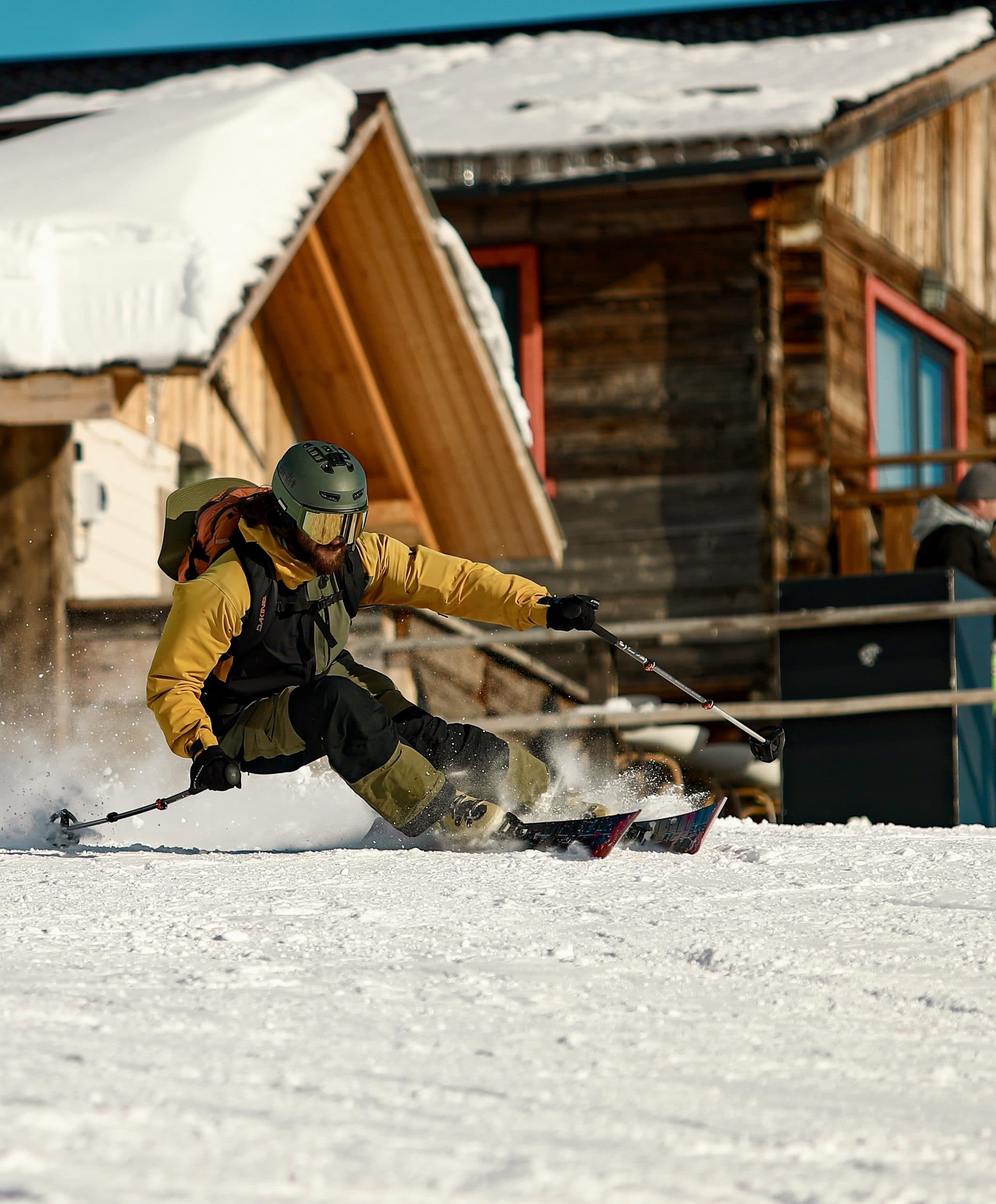 Skier carving past snow-covered mountain cabins